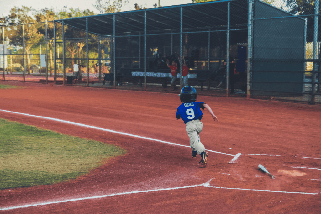 a photo of a kid playing baseball. he just hit the ball and is running to first base.