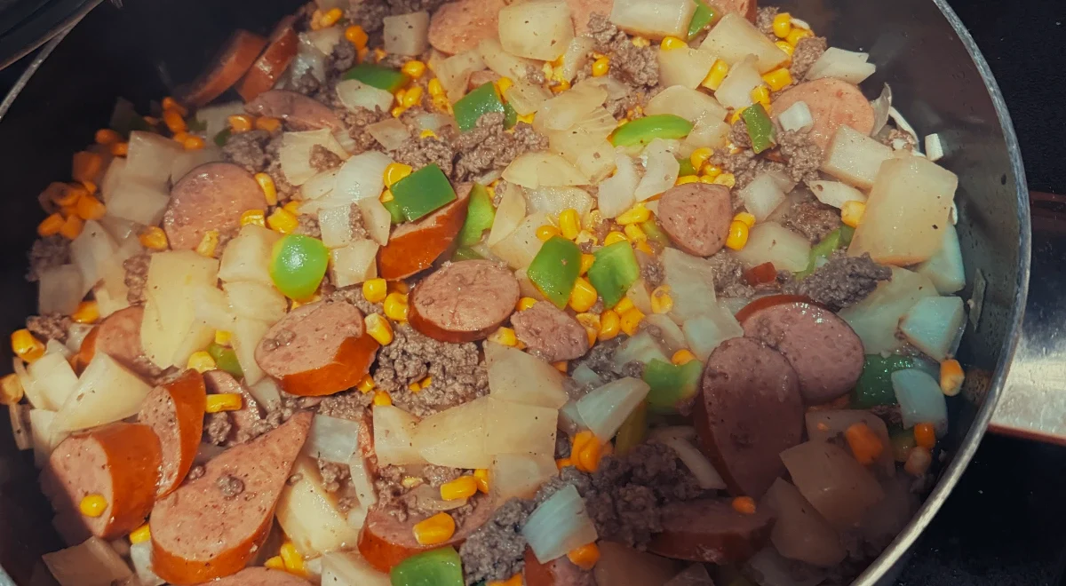 Firehouse stew cooking with ground beef, kielbasa, potatoes, corn, and green peppers.