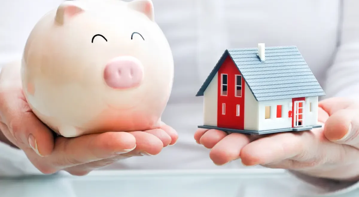 A photo of a piggy bank and a model of a home implying ways to save money as a homeowner